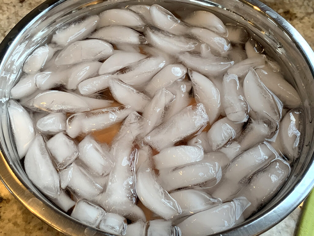A silver bowl filled with ice and water to create an ice bath for hard boiled eggs.