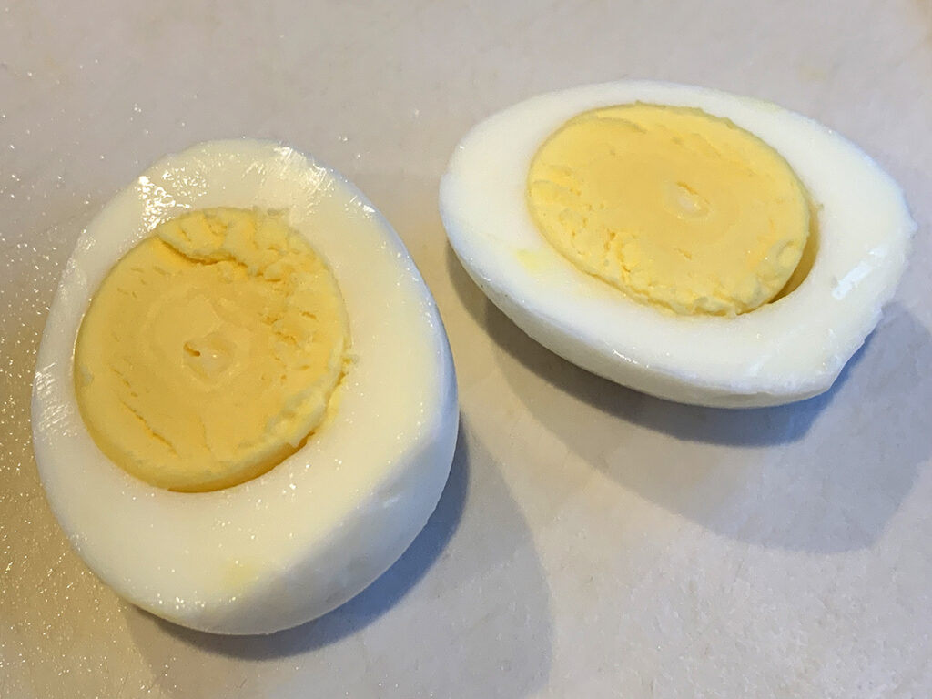 One hard boiled egg, cut in half laying on a white cutting board.