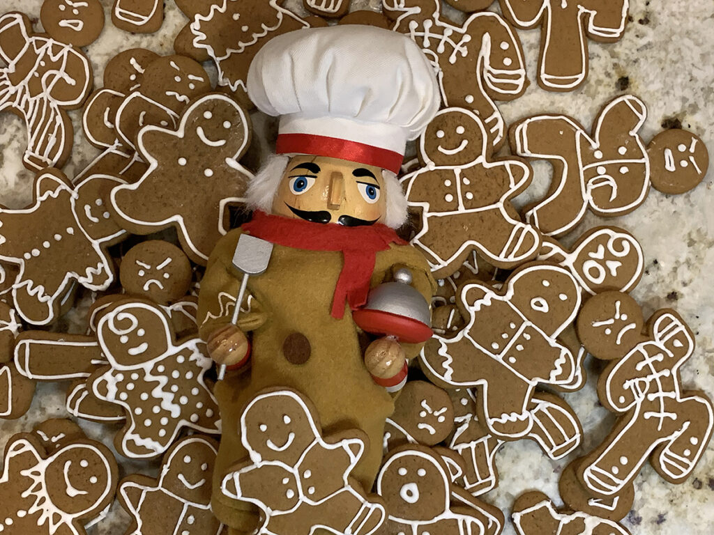 Pile of cute gingerbread men cookies with a nutcracker who looks like a chef, wearing a gingerbread man costume in the middle of the pile. 