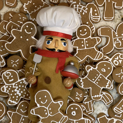 Pile of cute gingerbread men cookies with a nutcracker who looks like a chef, wearing a gingerbread man costume in the middle of the pile.