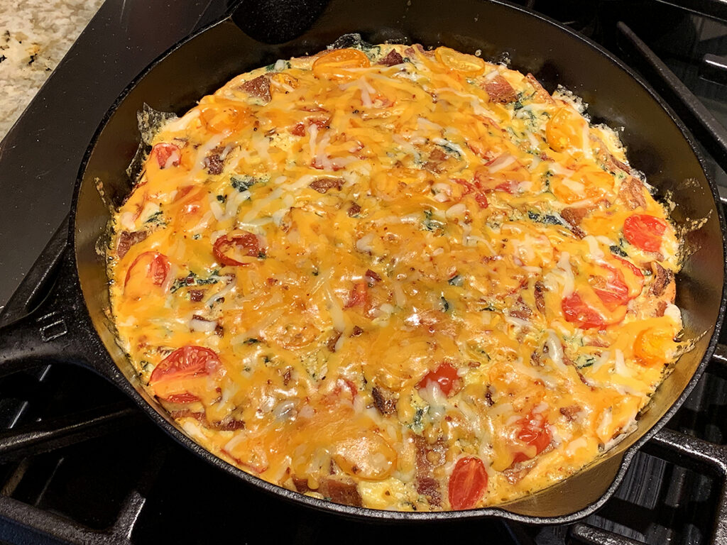 Baked egg frittata in an iron skillet layered with melted shredded cheddar cheese.