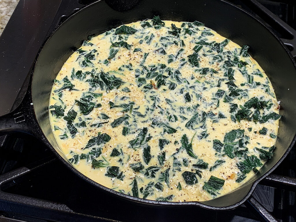 Beaten eggs in an iron skillet with chopped green stinging nettles layered on top.