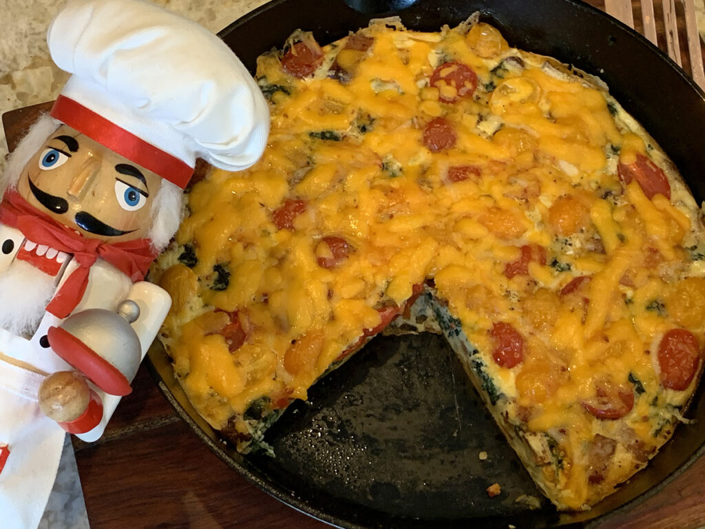 Baked egg frittata in an iron skillet with one piece missing. There's a nutcracker in the foreground who looks like a nutcracker.