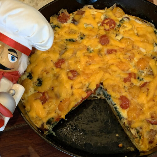 Baked egg frittata in an iron skillet with one piece missing. There's a nutcracker in the foreground who looks like a nutcracker.