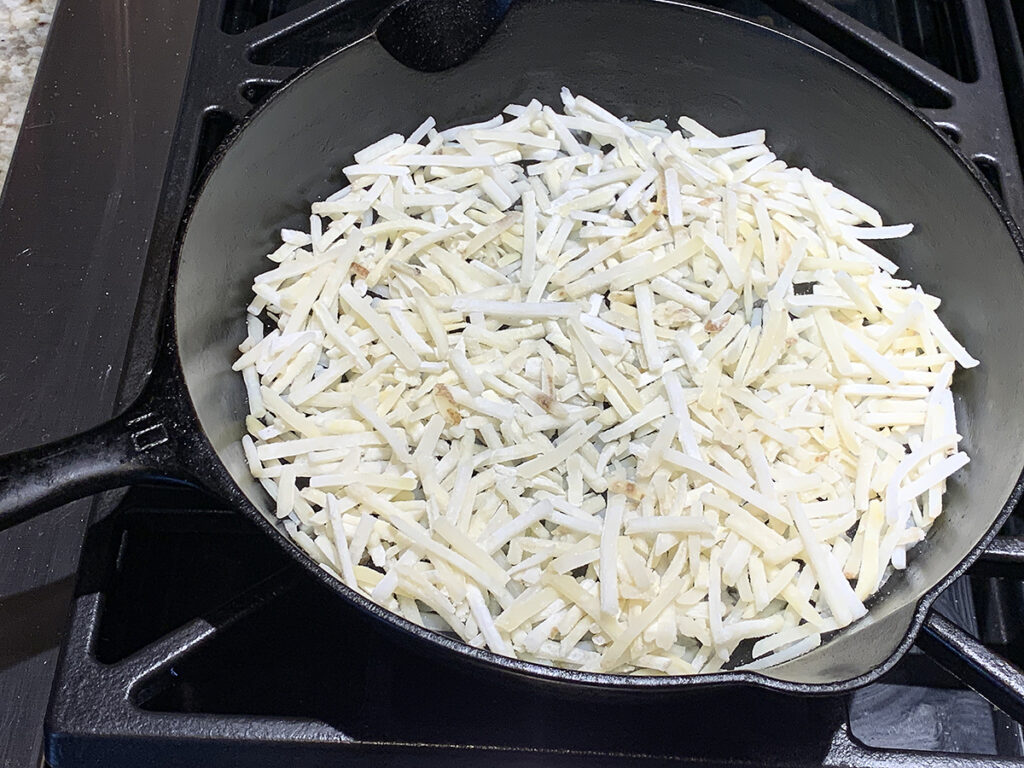 Frozen hash browns covering the bottom of an iron skillet.
