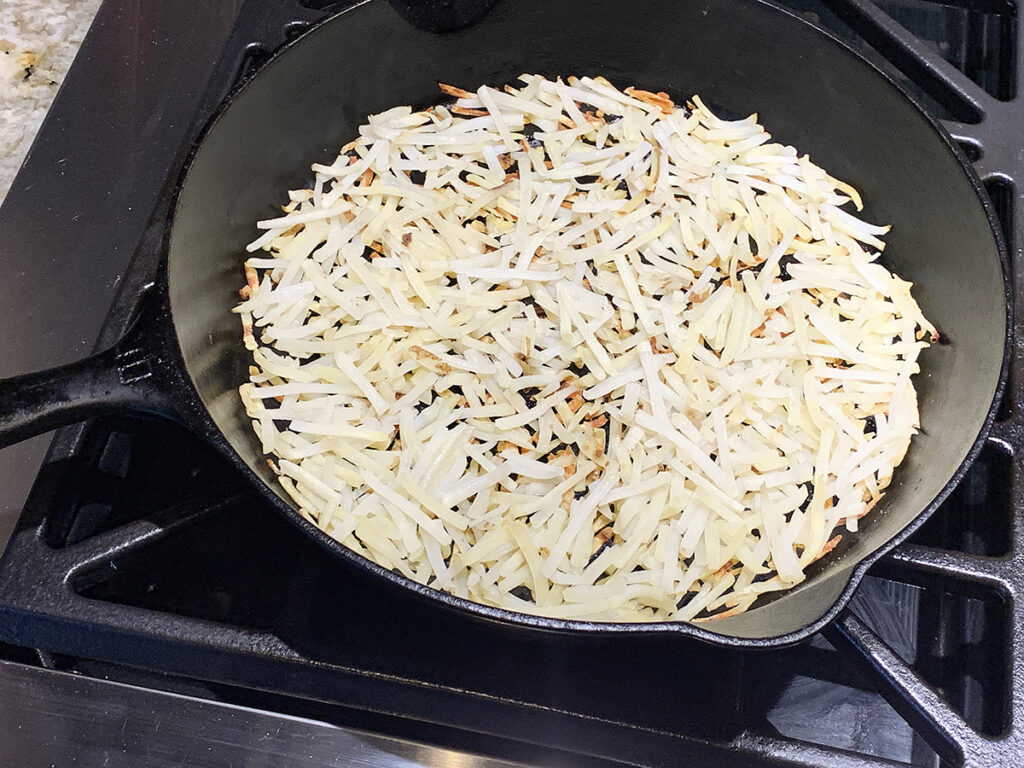 Cooked hash browns covering the bottom of an iron skillet.